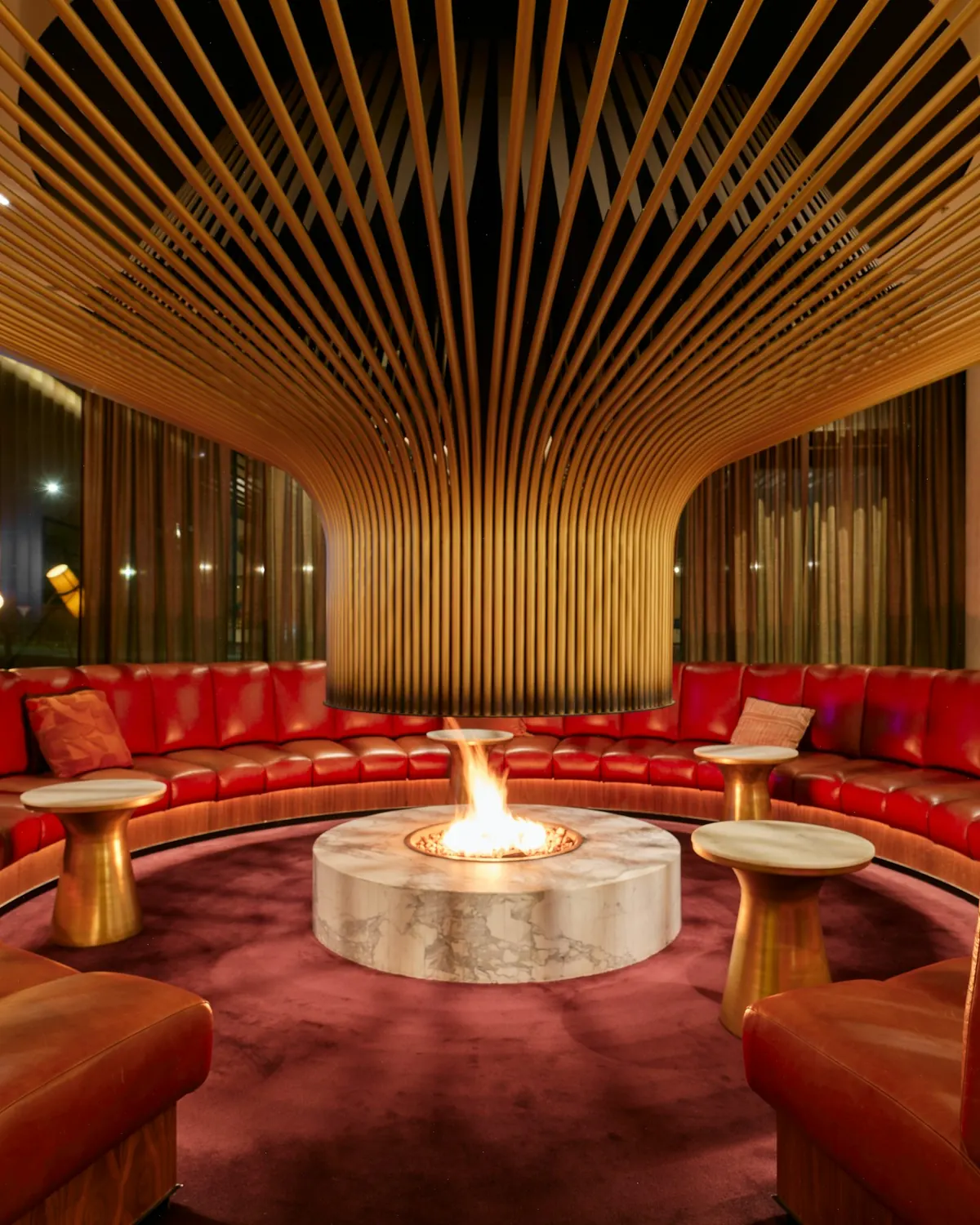 A warm private lounge with a round fire pit and curved red seating